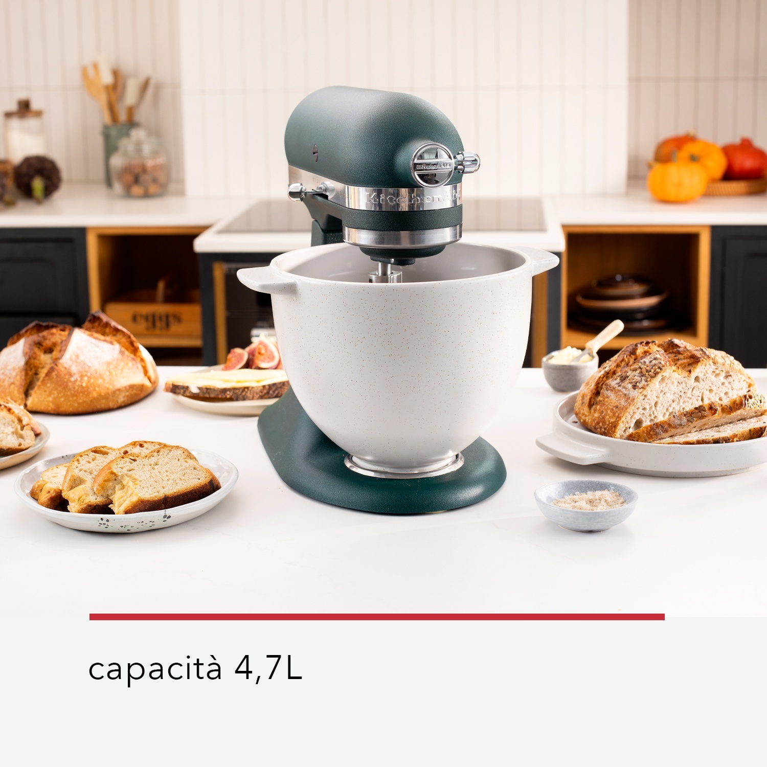 Ein grüner KitchenAid-Küchenmixer mit Brot und Zutaten auf einer weißen Arbeitsplatte. Kürbisse und Brot im Hintergrund.