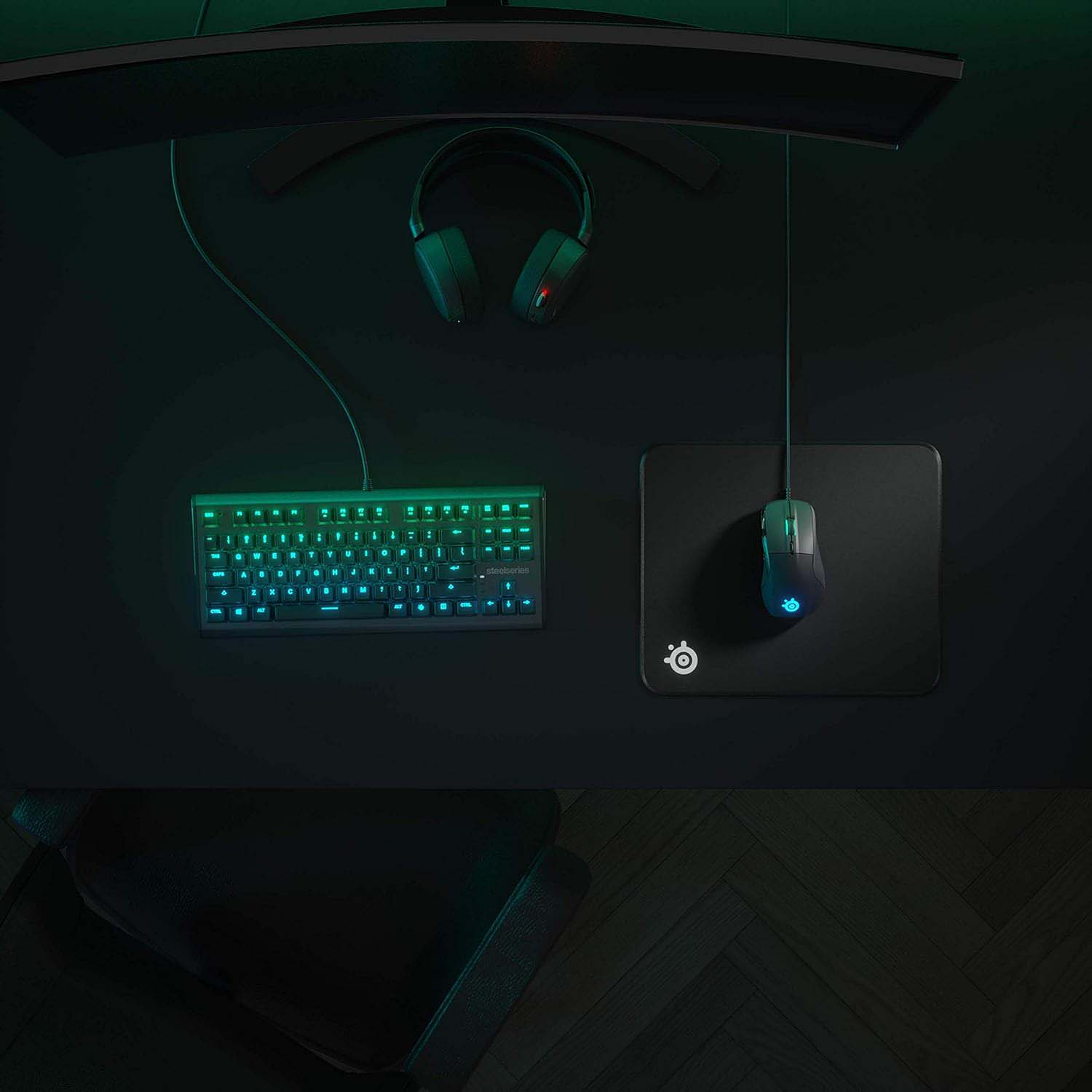 Une configuration de jeu avec clavier, souris, casque et tapis de souris sur un bureau sombre. Clavier et souris éclairés.