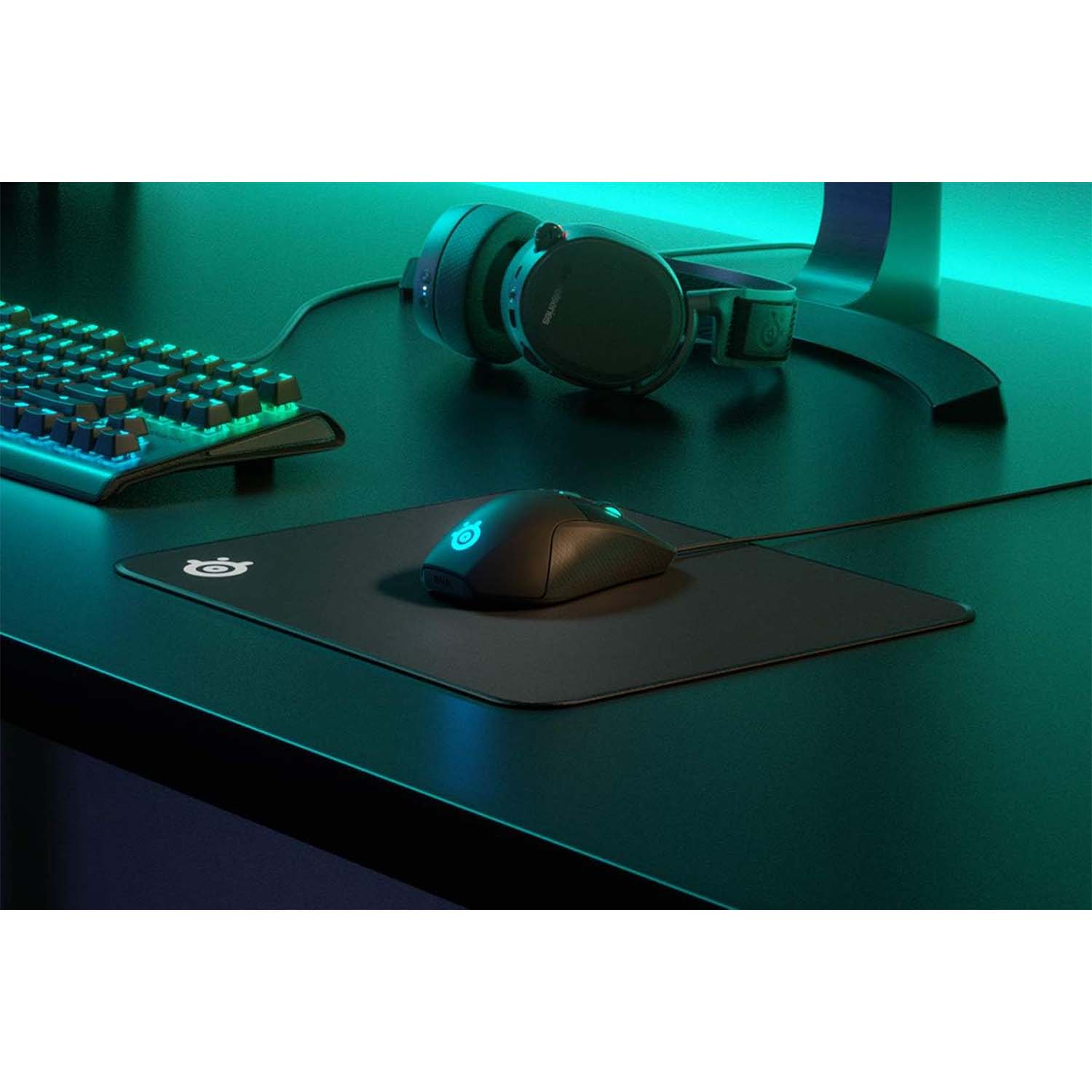 Une configuration de jeu avec une souris, un tapis de souris, un clavier et un casque sur un bureau noir. La scène a un éclairage bleu-vert.