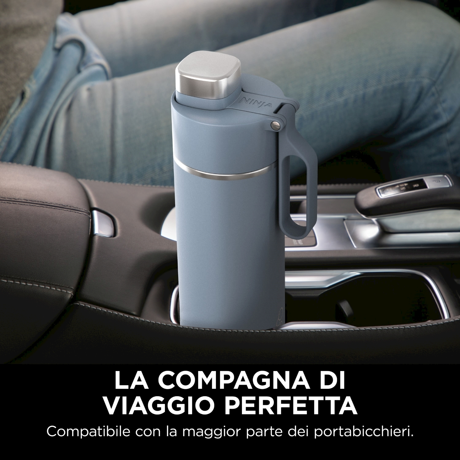 Una borraccia grigia Ninja è nel portabicchieri di un'auto. Le gambe di una persona sono sullo sfondo, il testo sottostante recita: Compagno di viaggio perfetto.