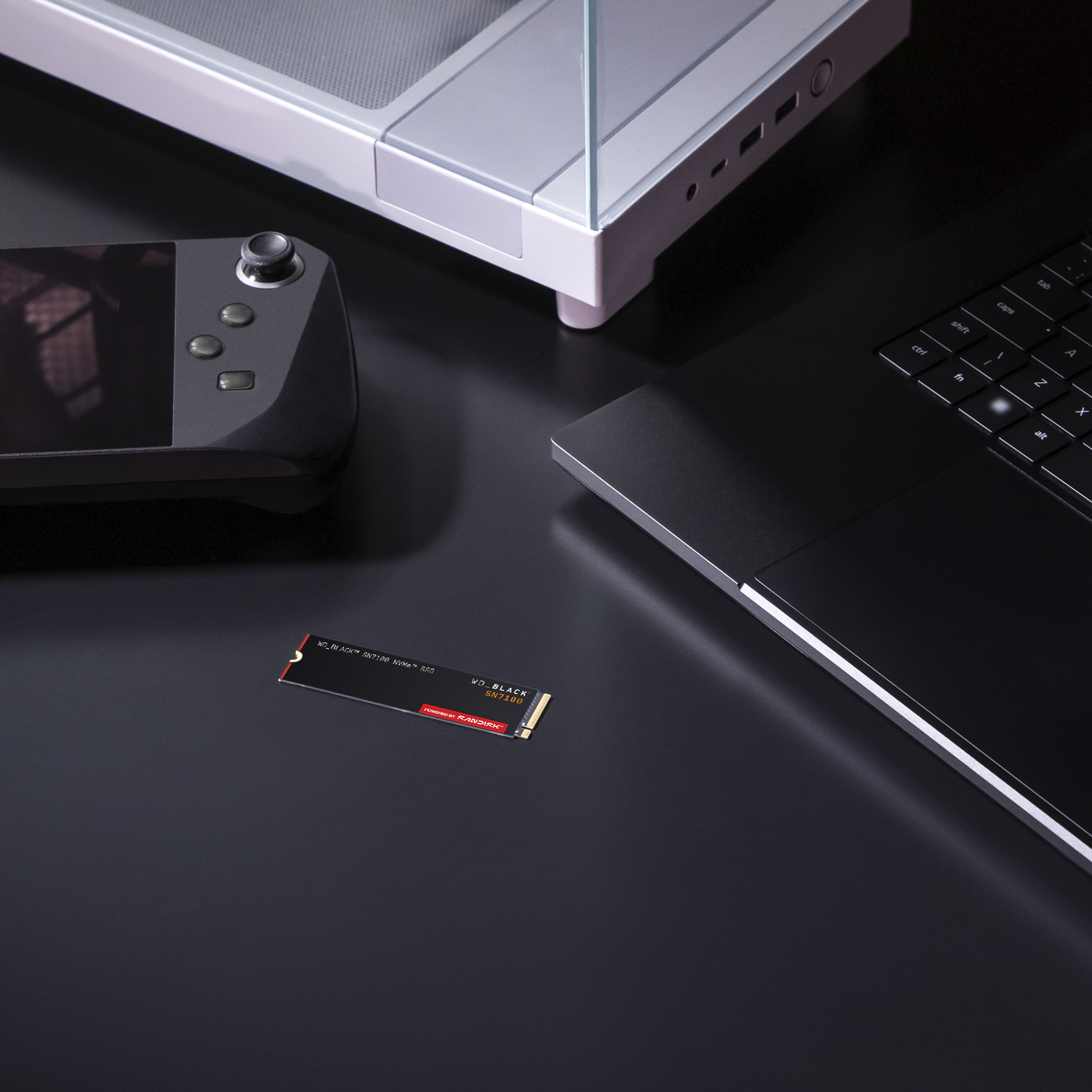 Czarny laptop, konsola do gier i dysk SSD na ciemnej powierzchni. Dysk SSD ma czerwony tekst.