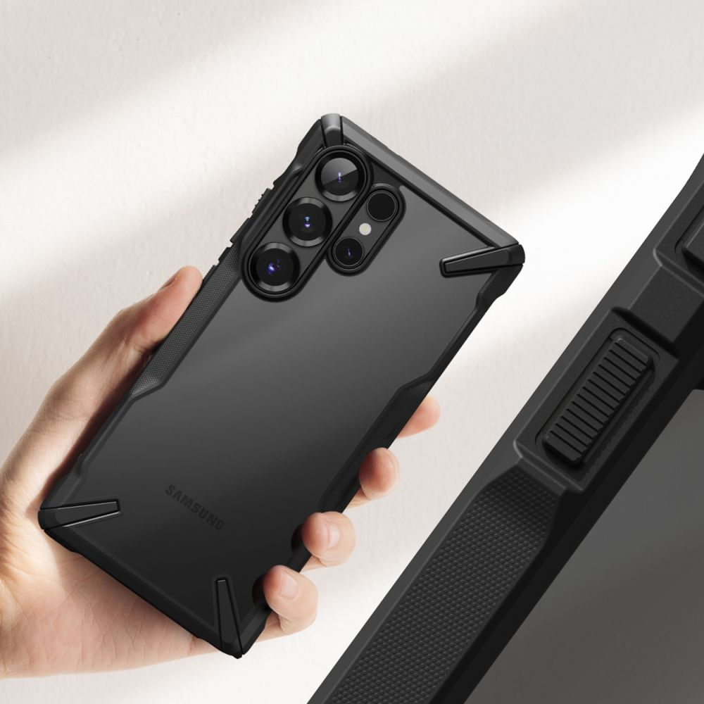 Una mano tiene un telefono nero con una custodia protettiva. Il telefono ha più lenti della fotocamera. A destra, una custodia nera strutturata.
