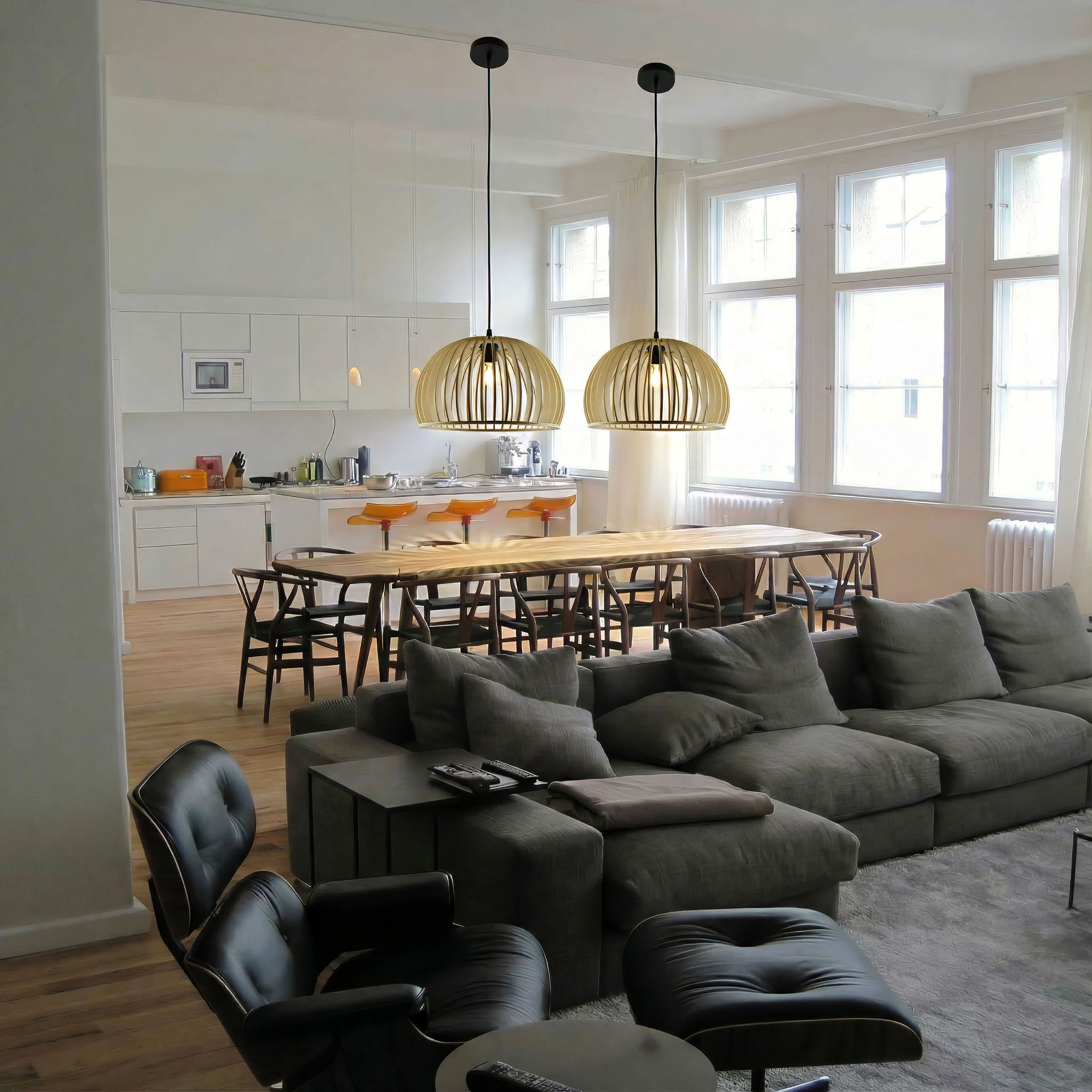 Offener Wohnraum mit Küche, Ess- und Wohnbereich. Zwei Pendelleuchten hängen über einem Esstisch. Graues Sofa vorhanden.