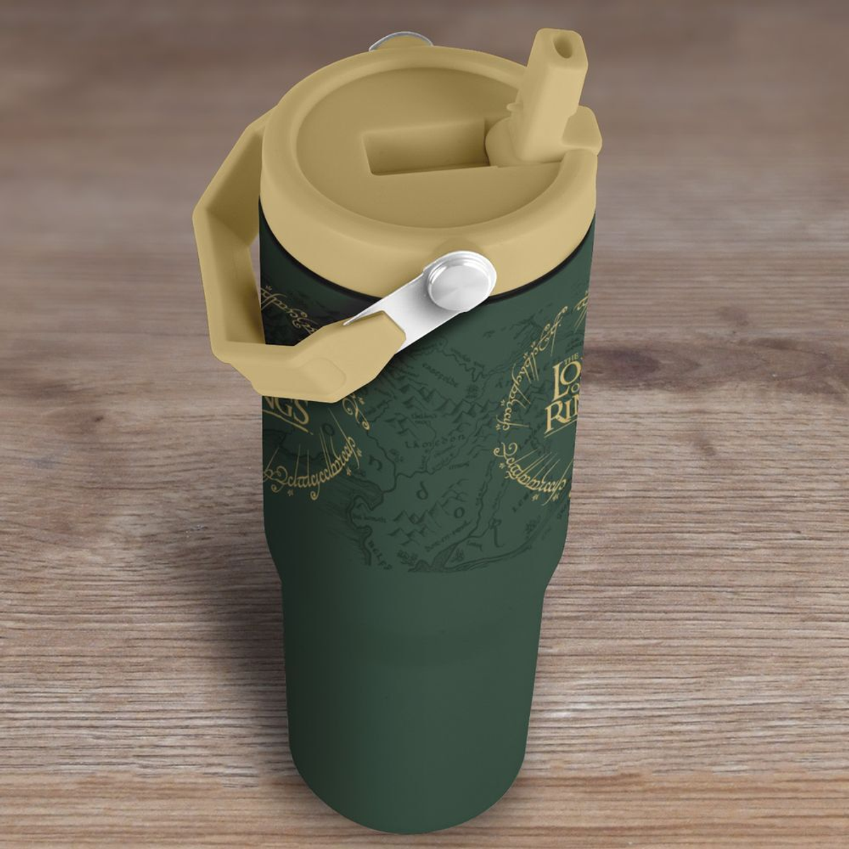 Un termo verde con diseño de mapa y la frase "Lord of the Rings". Tiene tapa y asa color beige, sobre una superficie de madera.