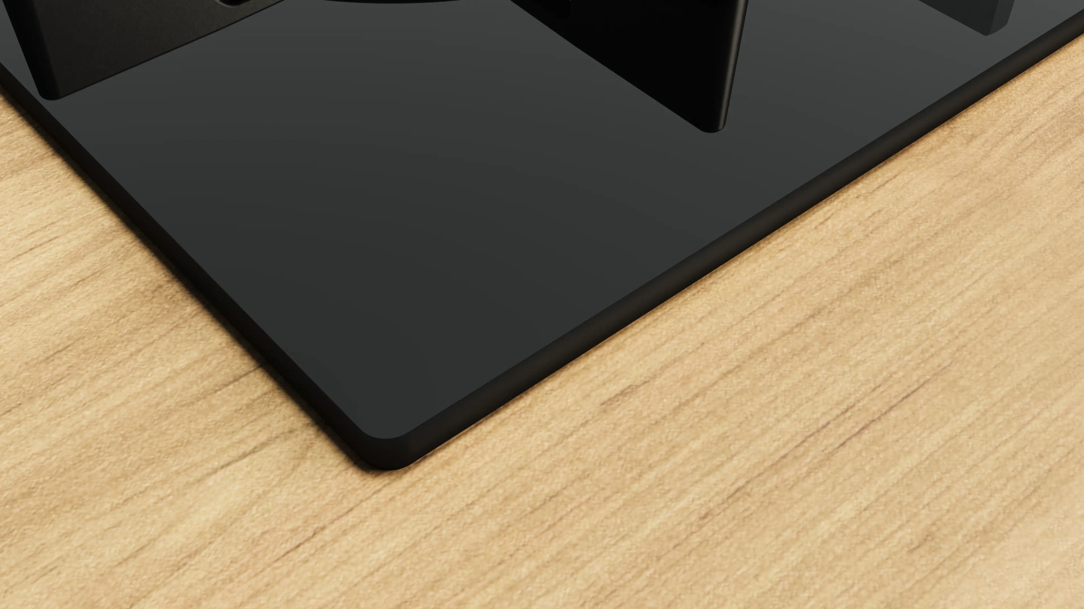 Zbliżenie czarnej, błyszczącej powierzchni, prawdopodobnie płyty kuchennej, na tle jasnego usłojenia drewna. Blat ma zaokrąglone rogi.