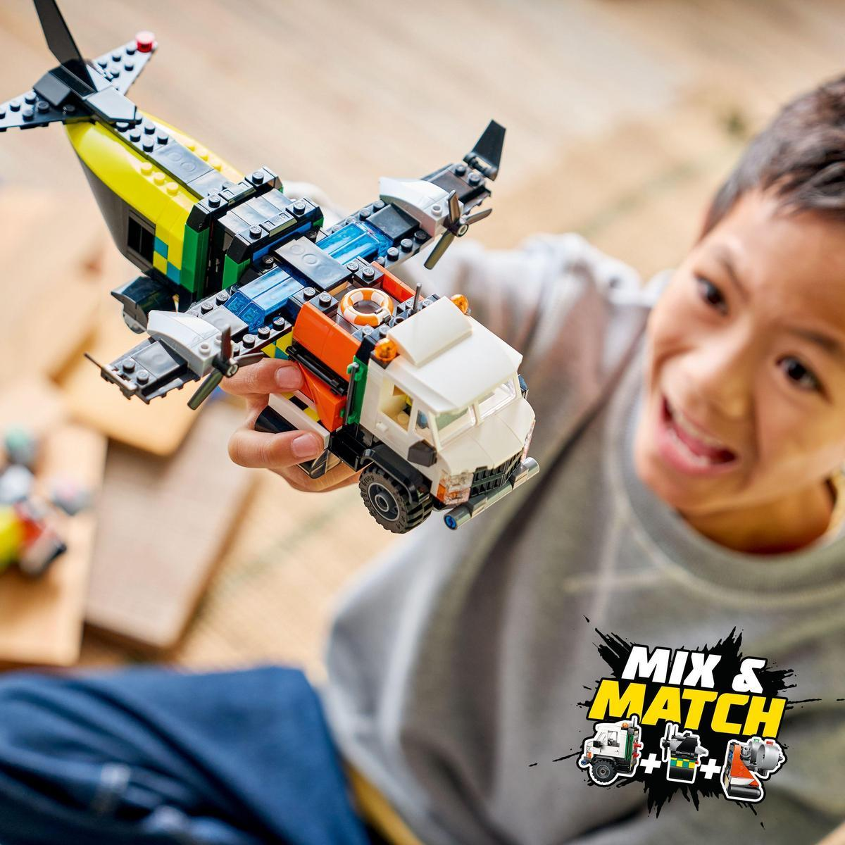Chłopiec trzyma zabawkę Lego w postaci samolotu i ciężarówki. Samolot jest żółto-czarny, ciężarówka biało-pomarańczowa. Chłopiec się uśmiecha.