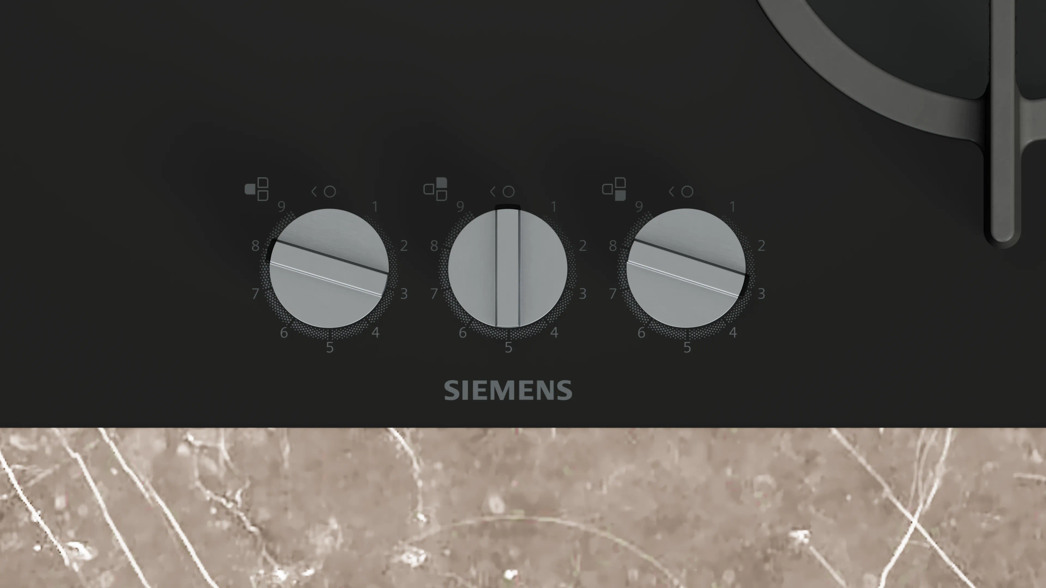 Un primo piano di un piano cottura Siemens nero con tre manopole di controllo. I numeri 1-9 sono intorno a ogni manopola. Lo sfondo è un motivo in pietra.