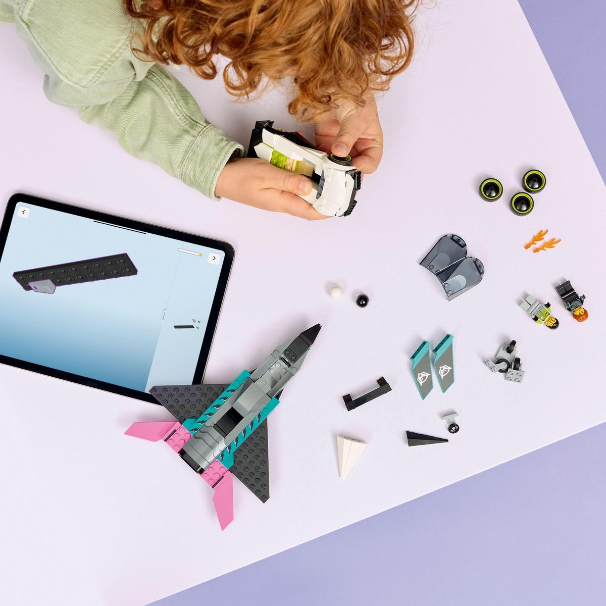Dziecko składa klocki Lego, w tym odrzutowiec, samochód i koła, prowadzone przez tablet na fioletowej powierzchni. Różne części są rozrzucone.