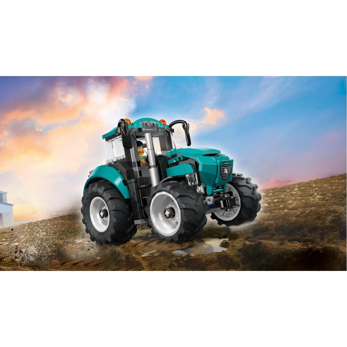 Teal zabawkowy traktor z dużymi oponami stoi na ziemnym wzgórzu na tle nieba w kolorze niebiesko-pomarańczowym.