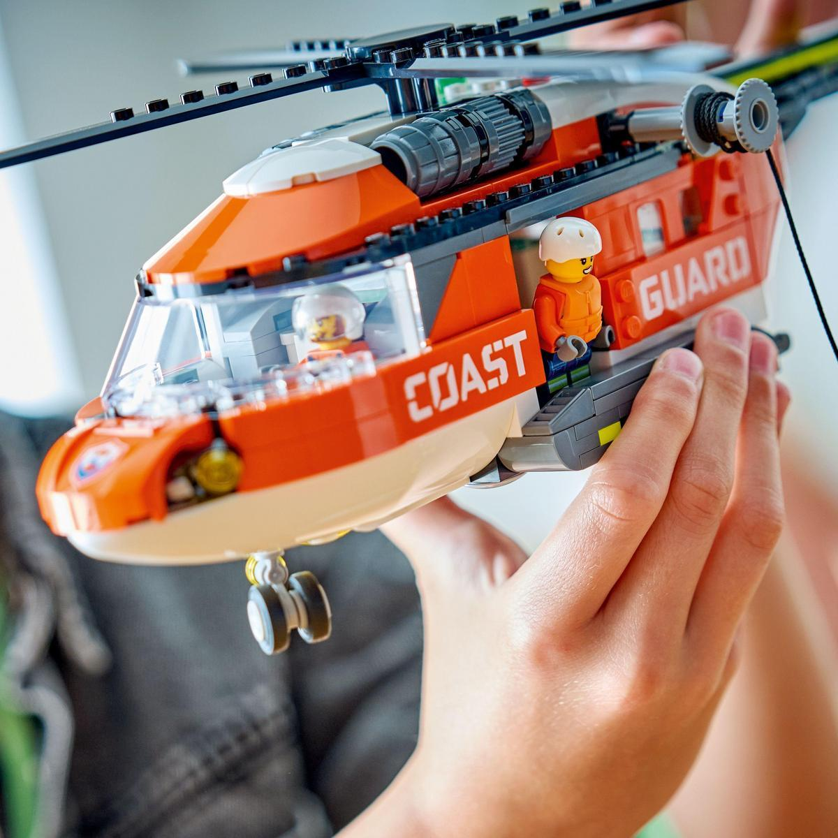 Dziecko trzyma pomarańczowo-biały helikopter Lego Coast Guard. W środku znajdują się dwie figurki Lego. Helikopter ma obracający się wirnik.