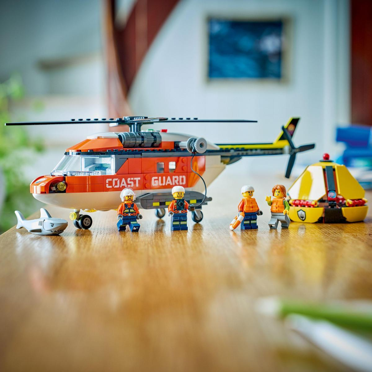 Zestaw Lego Coast Guard z helikopterem, rekinem i figurkami ratowników na drewnianej powierzchni. Obecna jest również żółta łódź ratunkowa.