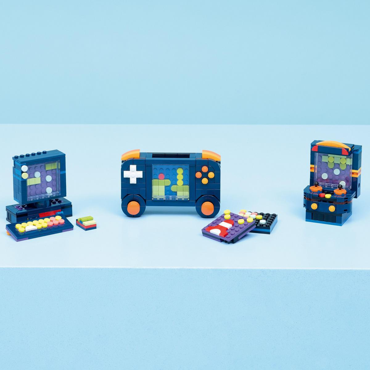 Trzy zabawki w postaci konsol do gier z klocków na niebieskiej powierzchni. Jedna ma ekran, przyciski i koła. Inne są podobne.