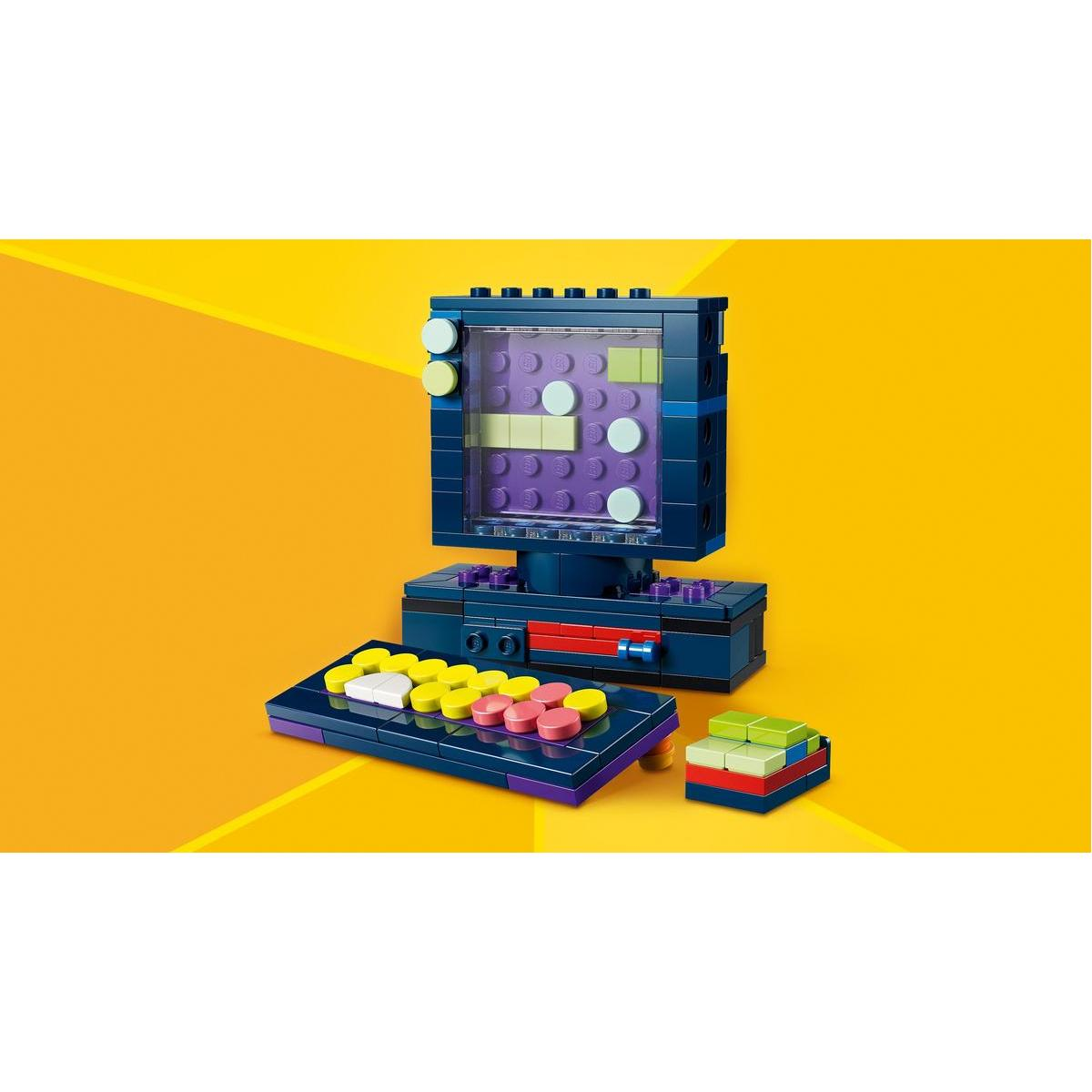 Komputer Lego z ekranem i klawiaturą, żółtymi i różowymi przyciskami oraz małym stosikiem klocków. Tło jest żółte.