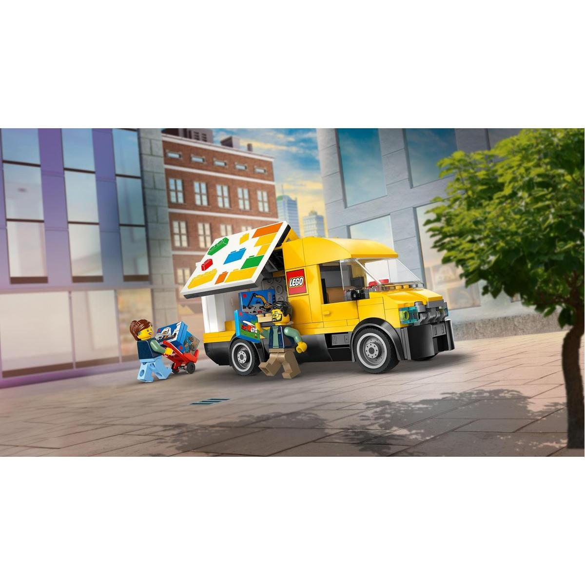 Żółta ciężarówka Lego z kolorową markizą. Dwie figurki Lego rozładowują pudełka. Budynki i drzewo w tle.