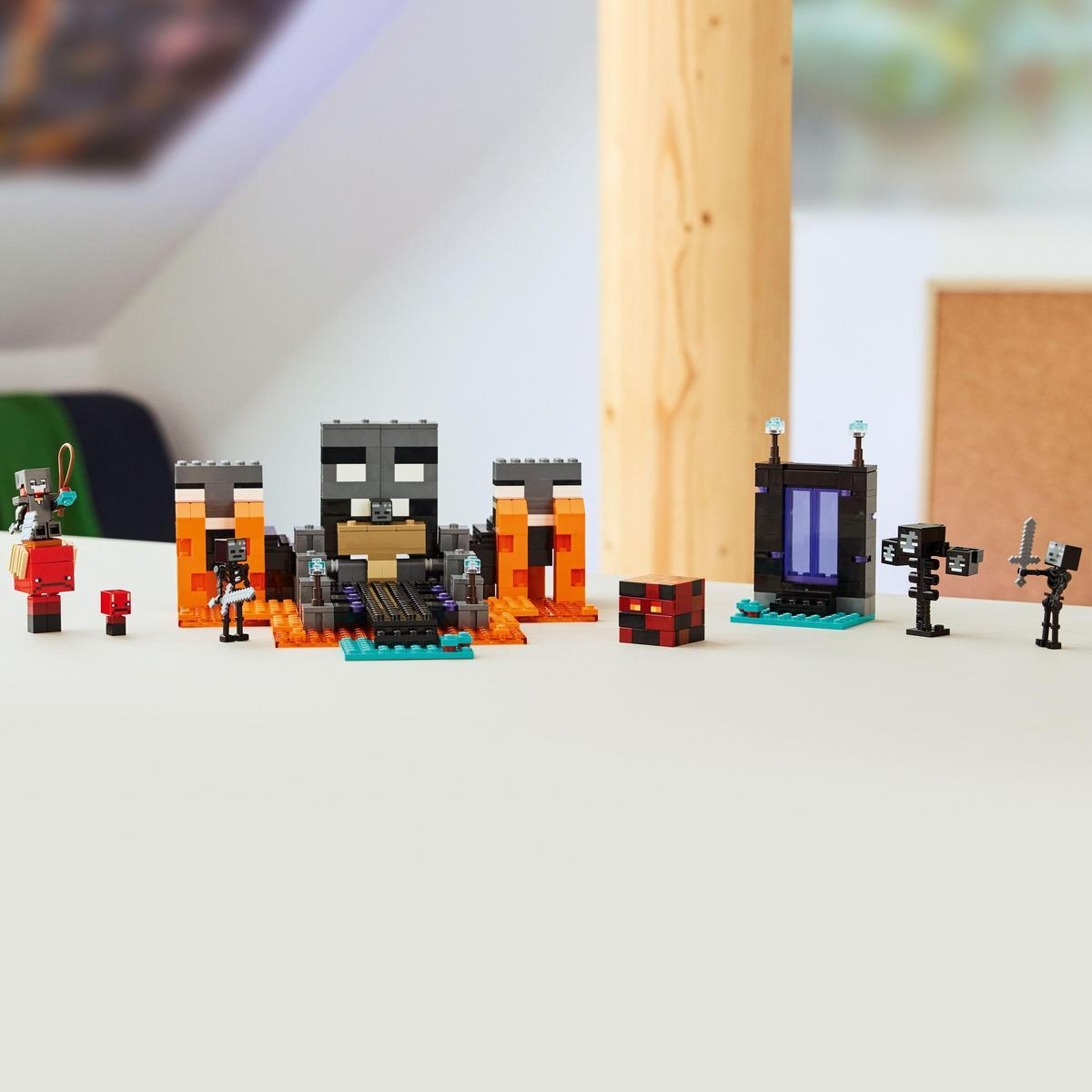 Zestaw Lego z różnymi figurkami i strukturami z Minecraft, w tym fortecą, portalem i kilkoma postaciami na białej powierzchni.