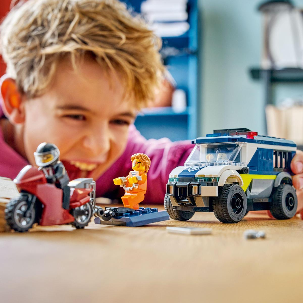 Dziecko uśmiecha się do zabawek policyjnych Lego: motocykla, więźnia i vana. Scena rozgrywa się na drewnianym stole.