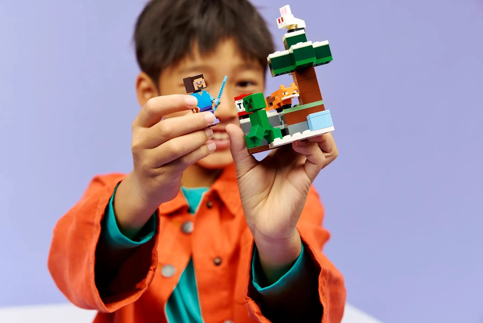 Dziecko trzyma figurki Lego Minecraft. Jedna figurka to Steve, druga to Creeper. Obecny jest również lis i królik.