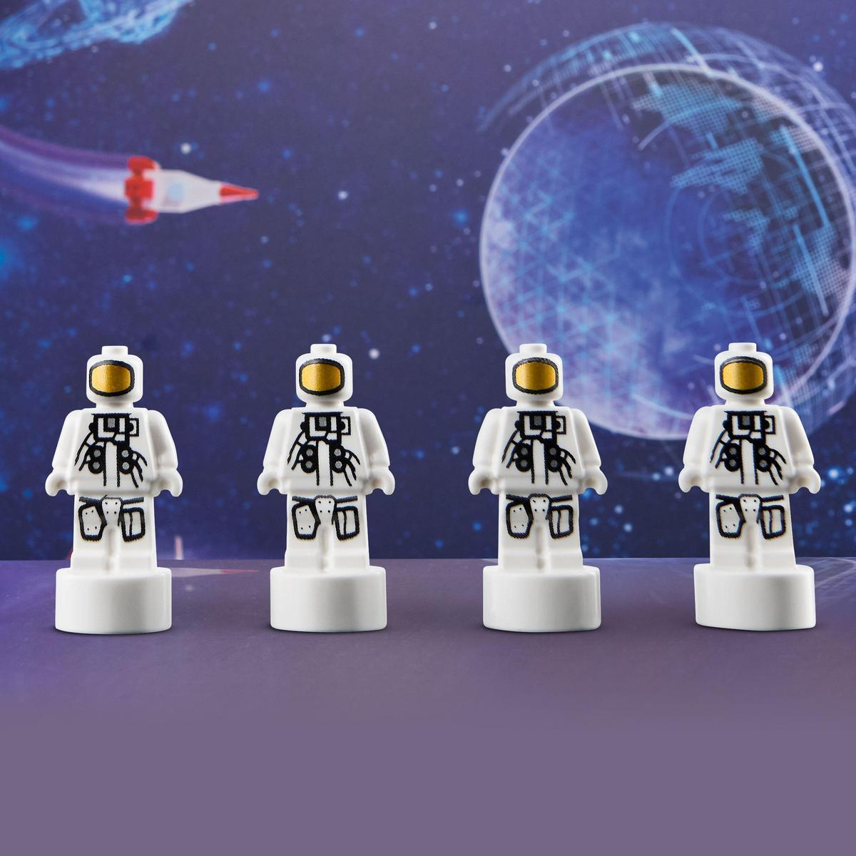 Czterech białych astronautów Lego na fioletowej powierzchni na tle kosmicznego z rakietą i planetą.