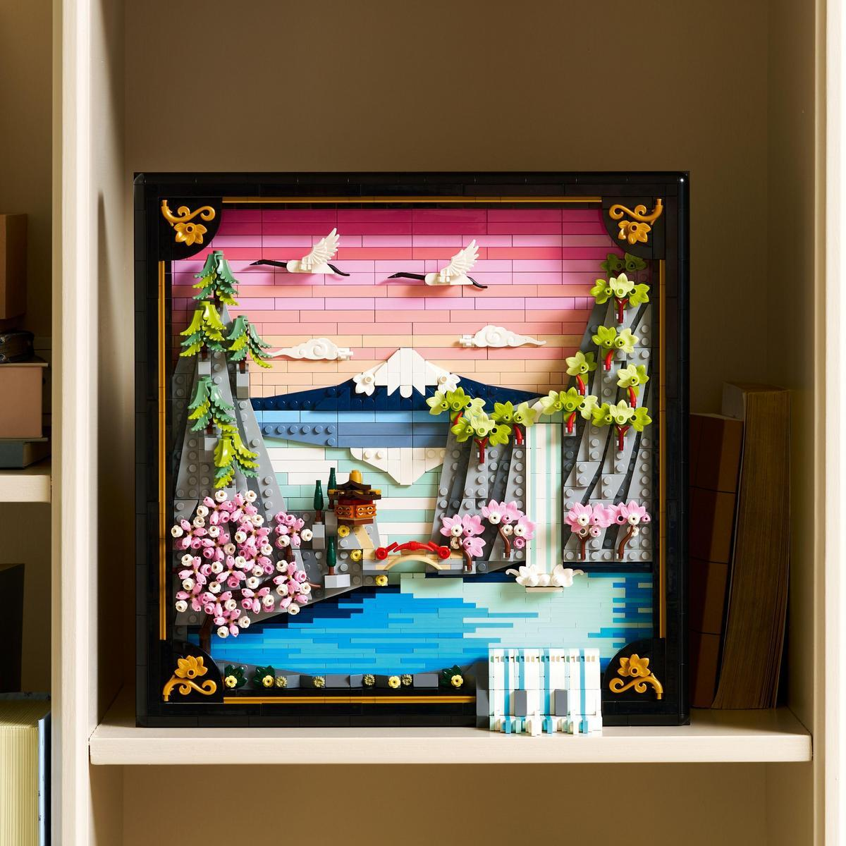 Diorama Lego z górą, jeziorem, drzewami i latającymi ptakami. Jest oprawione i wystawione na półce.