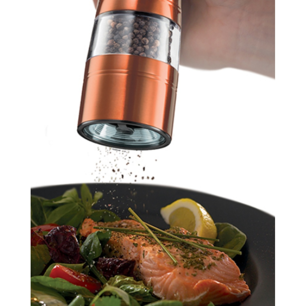 Bir el, somon ve salata üzerine karabiber öğütüyor. Karabiber değirmeni bakır renginde. Tabakta salata, somon ve limon var.