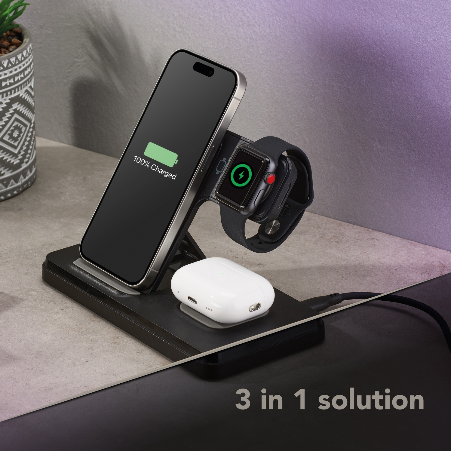 Una estación de carga para teléfono, reloj y auriculares. El teléfono muestra 100% cargado. El reloj y los auriculares también se están cargando.