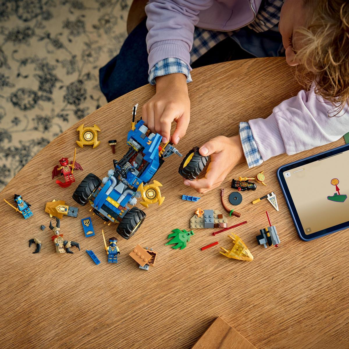 Dziecko składa samochód Lego na drewnianym stole. Klocki Lego i tablet z instrukcjami są rozrzucone.