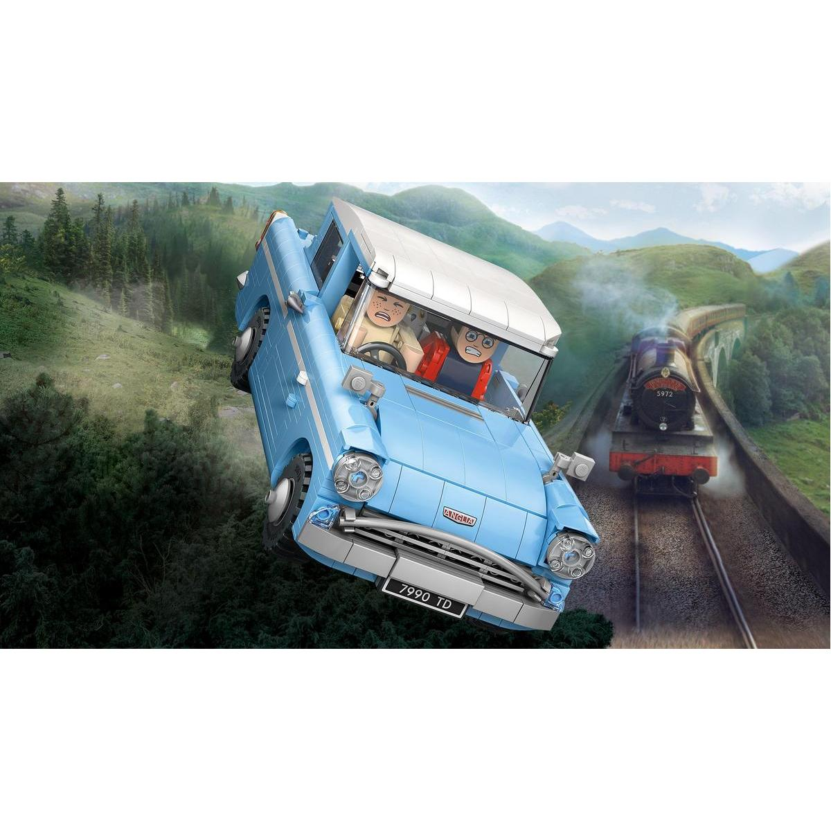 Niebieski samochód Lego leci, z dwiema postaciami w środku. Pociąg jedzie po torach w tle, w pobliżu mostu.