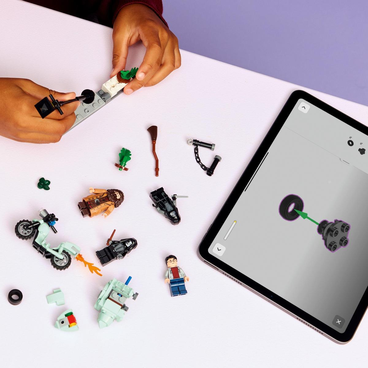 Ręce dziecka składają klocki Lego na stole. Różne figurki i części Lego są rozrzucone, z iPadem pokazującym instrukcje.
