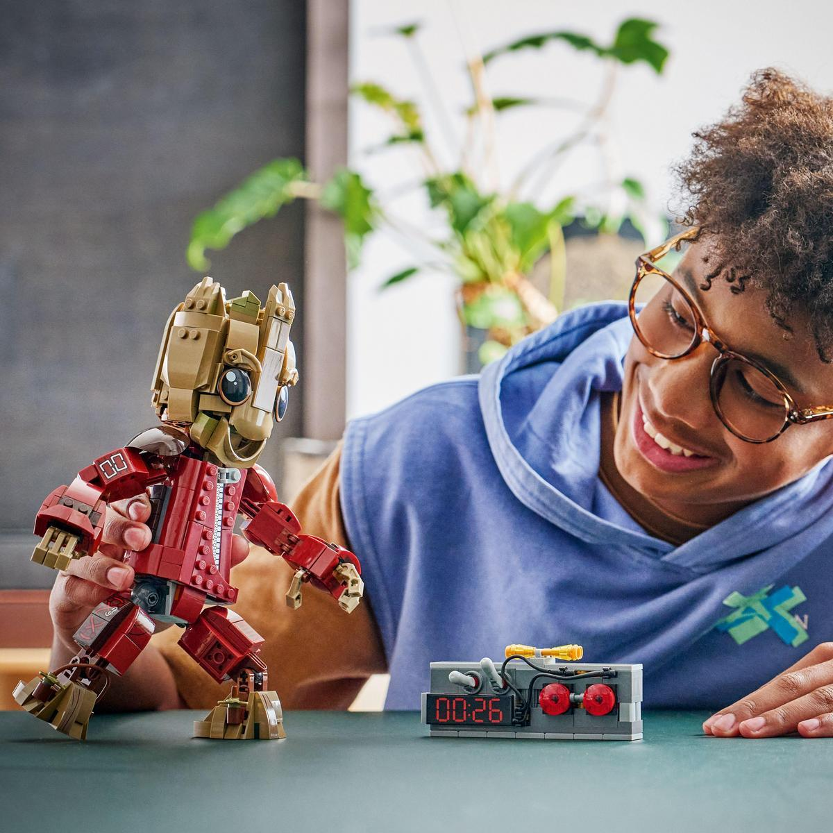 Osoba uśmiecha się do figurki Lego Groota. Na stole znajduje się timer Lego. W tle roślina.
