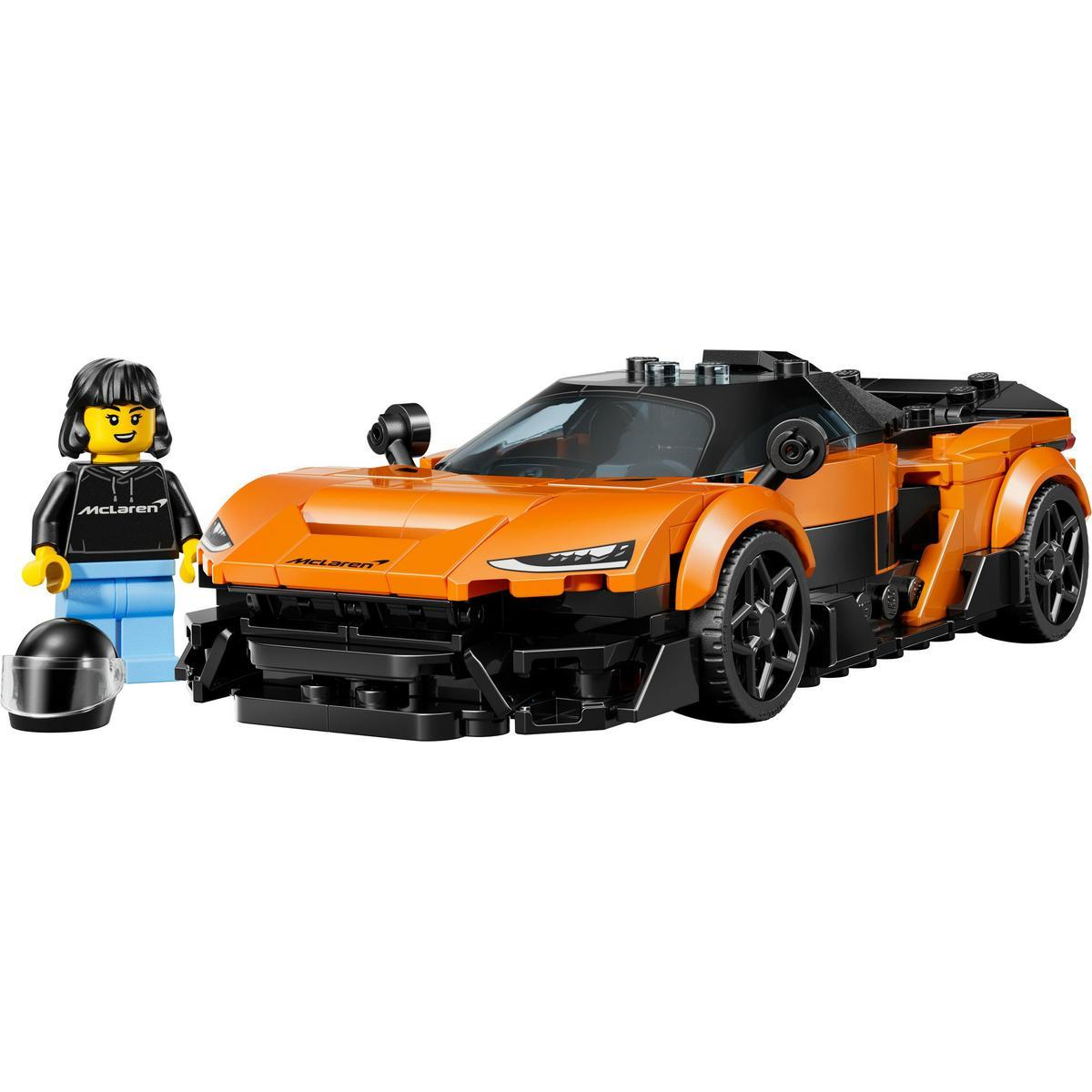 Model Lego pomarańczowo-czarnego samochodu McLaren obok minifigurki i czarnego kasku.