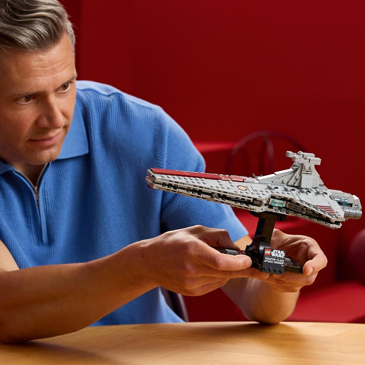 Mężczyzna trzyma model Lego Star Wars krążownika szturmowego klasy Venator. Ma na sobie niebieską koszulę, tło jest czerwone.