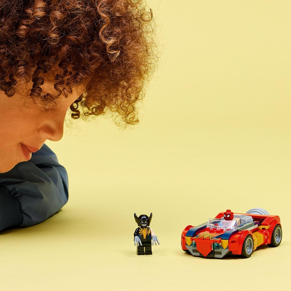 Osoba patrzy na zestaw Lego z samochodem i figurką. Samochód jest czerwony i żółty. Figurka jest czarna i żółta.