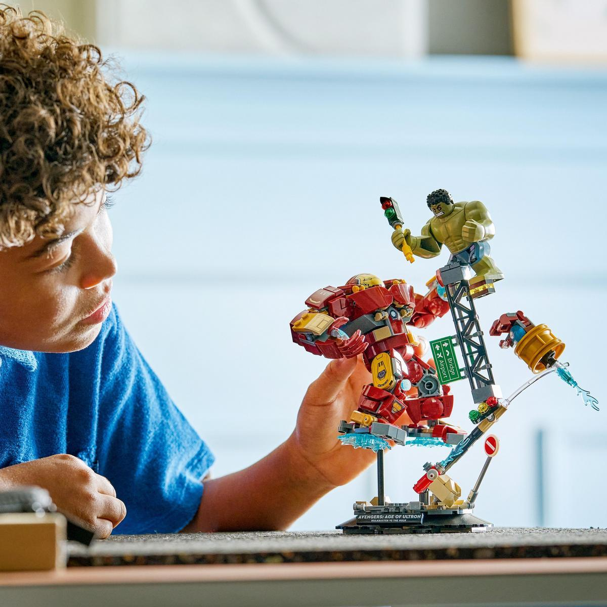 Chłopiec patrzy na zestaw Lego z Hulkiem i Iron Manem. Zestaw zawiera czerwono-żółtego Iron Mana, Hulka i scenę miejską.