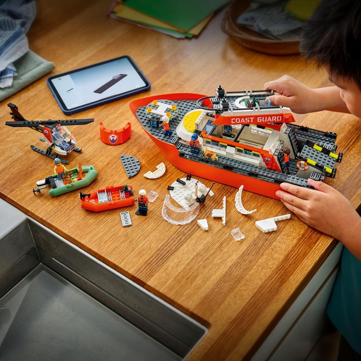 Dziecko buduje zestaw Lego Coast Guard. Zestaw zawiera helikopter, łodzie i figurki na drewnianej powierzchni.