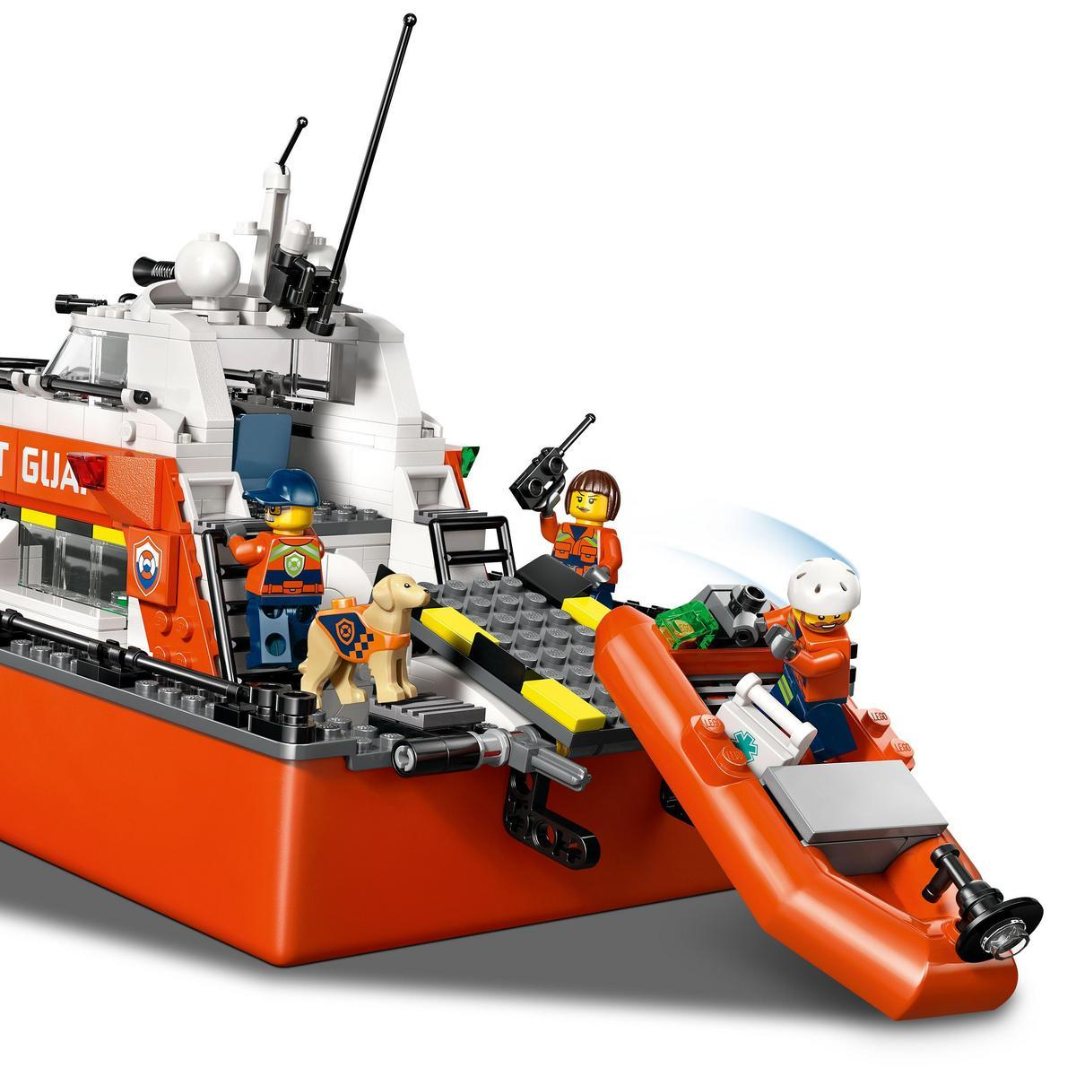 Statek Lego Straży Przybrzeżnej z figurkami i psem. Jedna figurka trzyma radio, druga jest w łodzi. Statek jest pomarańczowy i biały.