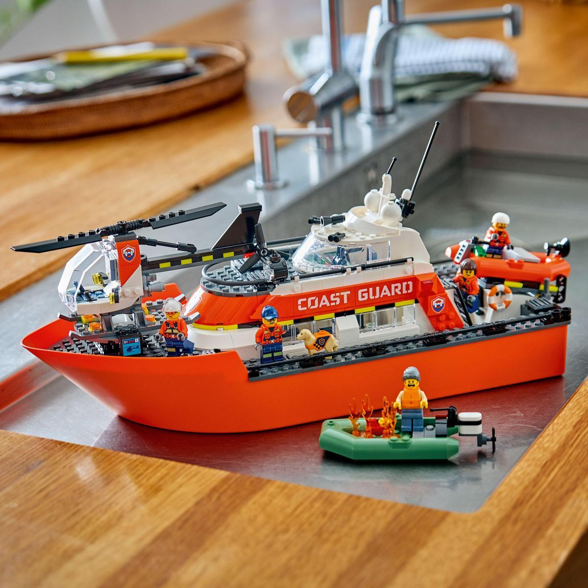 Statek straży przybrzeżnej Lego z helikopterem, łodzią ratunkową i kilkoma figurkami na drewnianej powierzchni.
