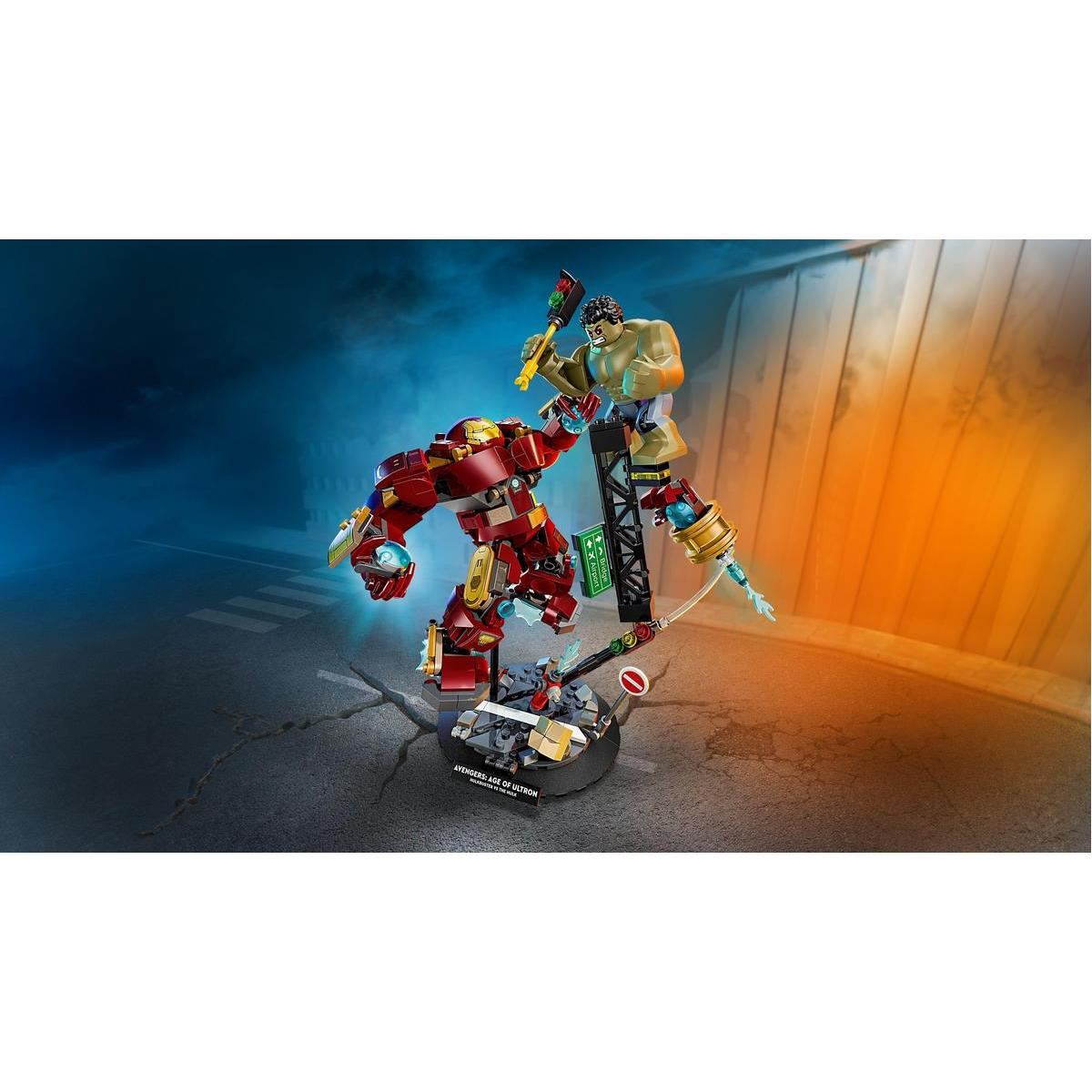 Zestaw Lego z postaciami Avengers. Czerwony robot i Hulk, stojący na pękniętej podstawie. Tło przedstawia ulicę i bramę.