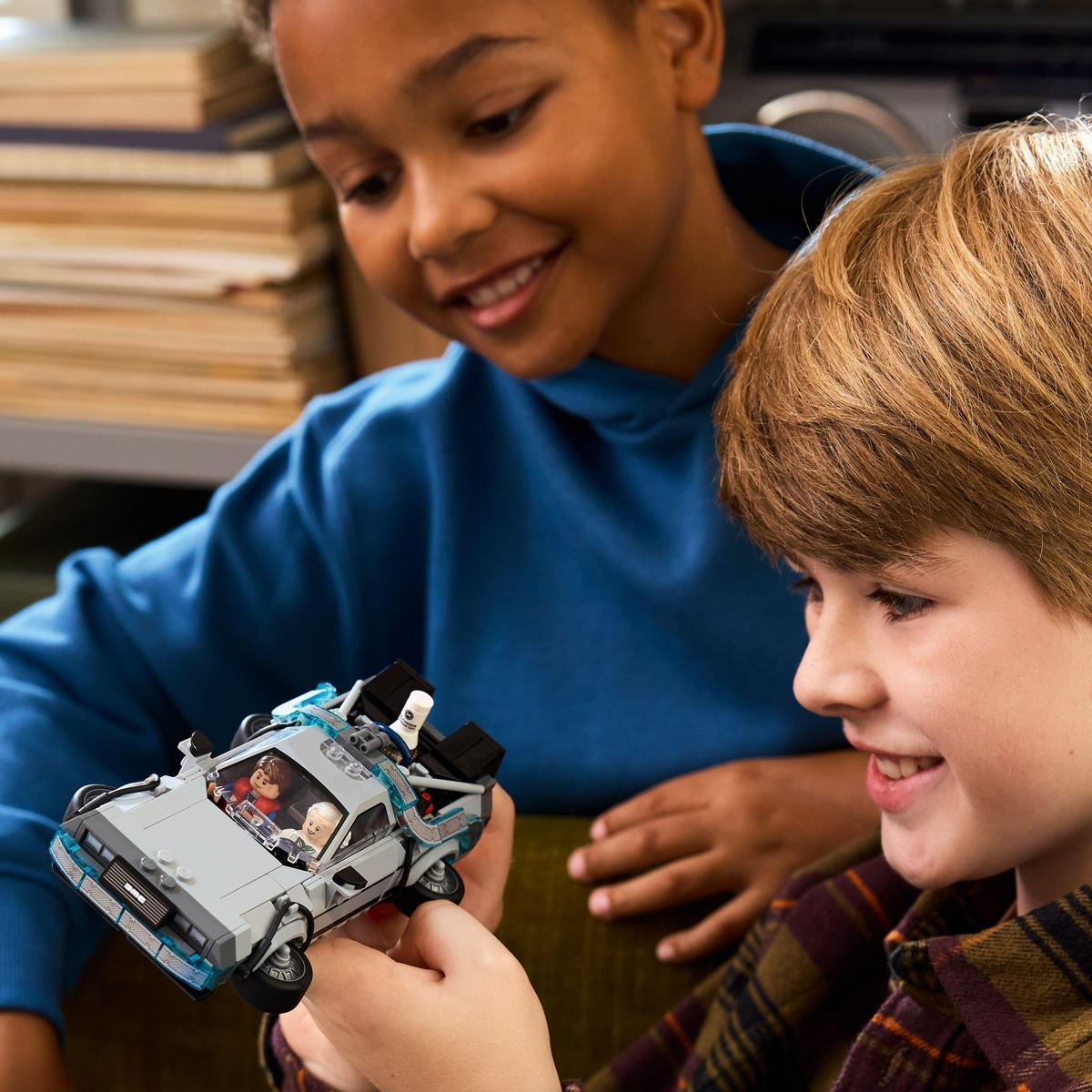 Dwóch chłopców patrzy na samochód DeLorean z Lego. Jeden trzyma samochód, uśmiechając się. Drugi uśmiecha się w tle, ubrany w niebieską koszulę.