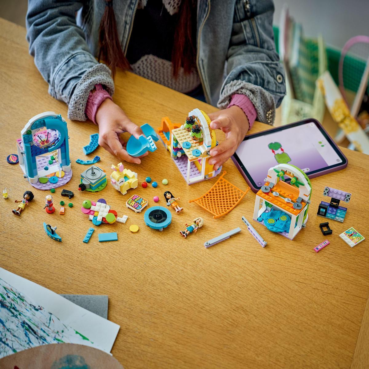 Osoba buduje zestaw Lego. Zestaw zawiera małą arkadę, trampolinę i kilka minifigurek na drewnianym stole.