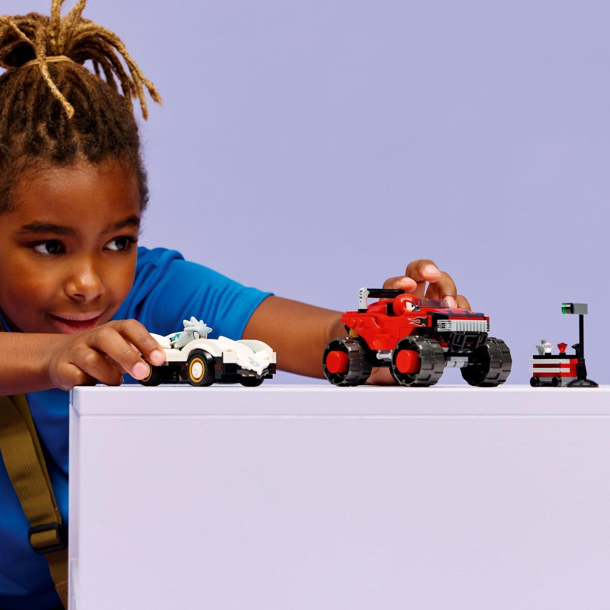Dziecko bawi się zabawkami: białym samochodem wyścigowym, czerwonym monster truckiem i miniaturowym warsztatem. Dziecko się uśmiecha.