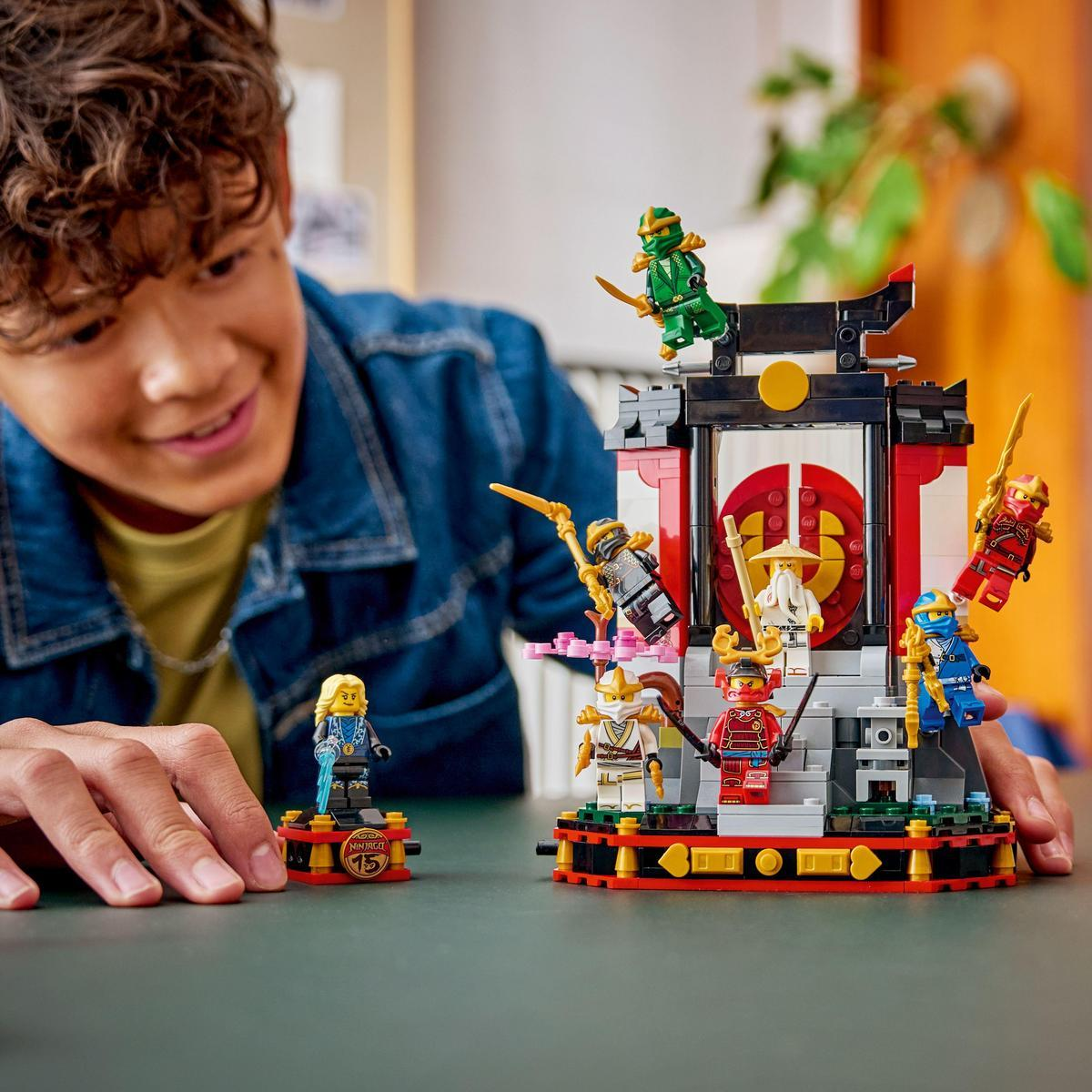 Chłopiec patrzy na zestaw Lego z figurkami ninja, świątynią i różnymi akcesoriami, wszystko na stole, w dobrze oświetlonym pokoju.
