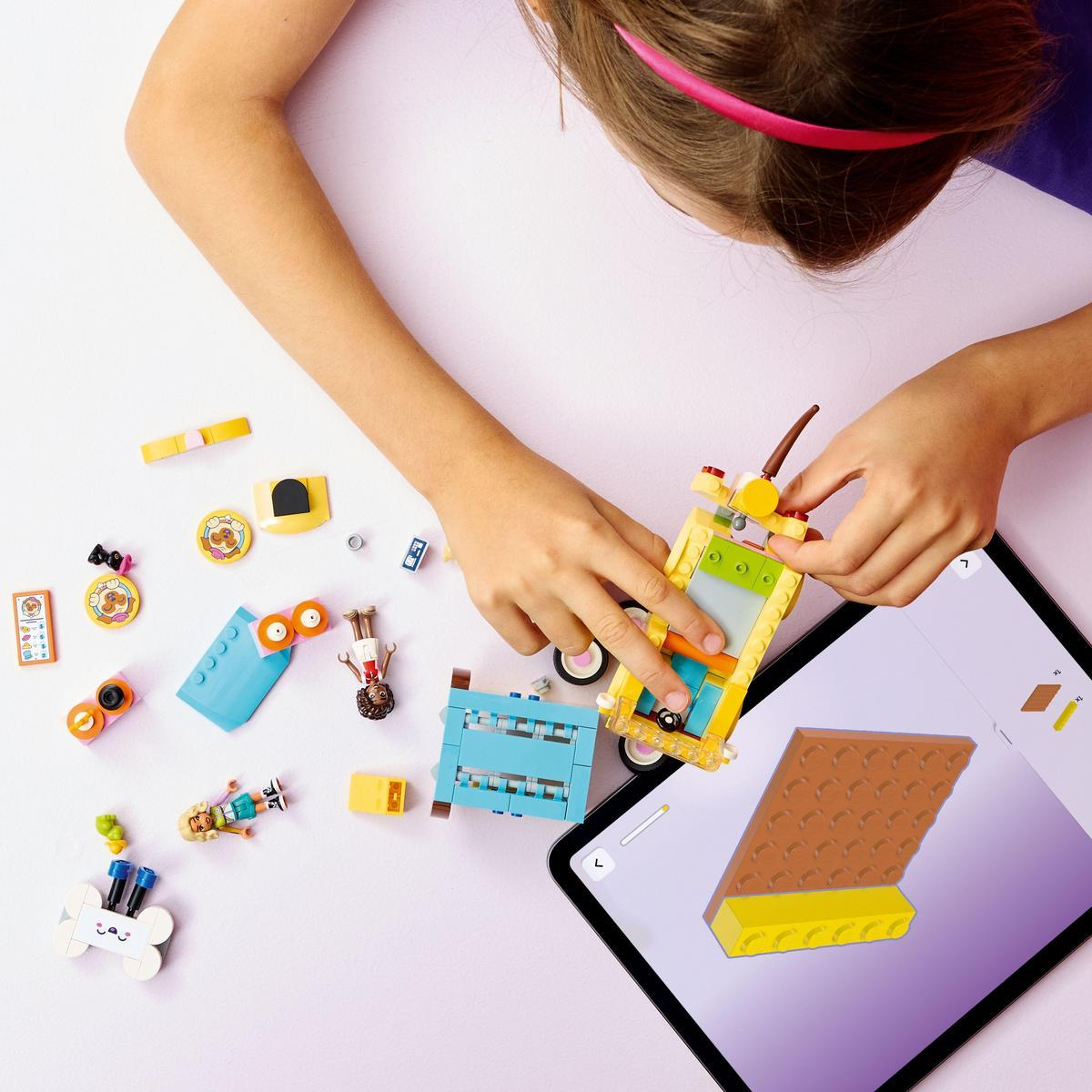 Dziewczyna składa zestaw Lego. Różne klocki Lego i tablet z instrukcjami leżą na białej powierzchni.