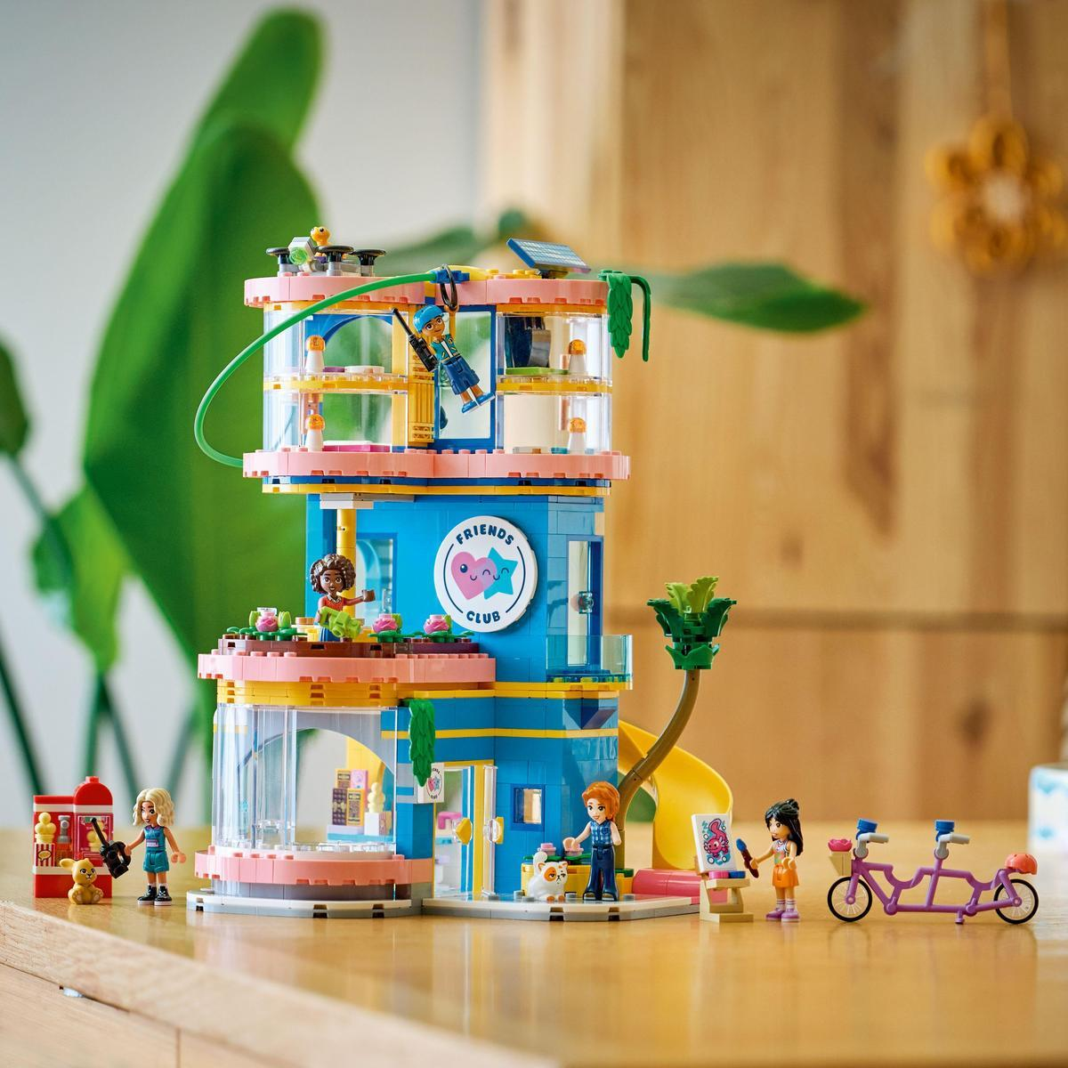 Edificio Lego Friends con personaggi, scivolo, tandem e scena di pittura. Sullo sfondo una pianta verde.
