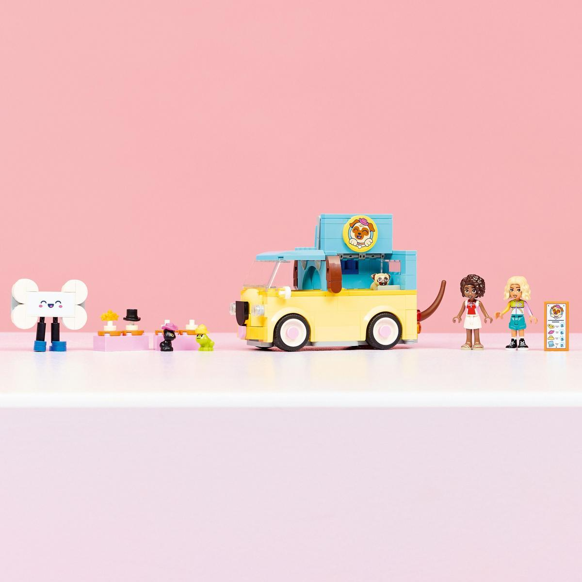 Żółta zabawka food truck z postaciami, kością, psem i dwiema dziewczynami na różowym tle.