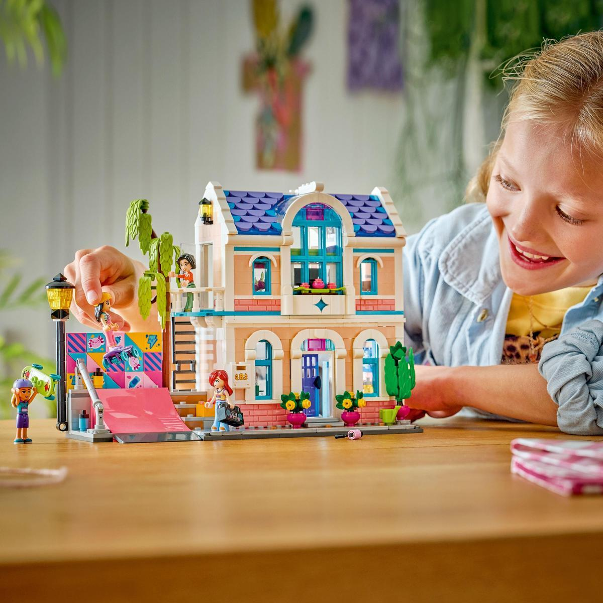 Una niña sonríe a una casa de Lego. La casa tiene techo azul, detalles rosas y figuras de Lego.