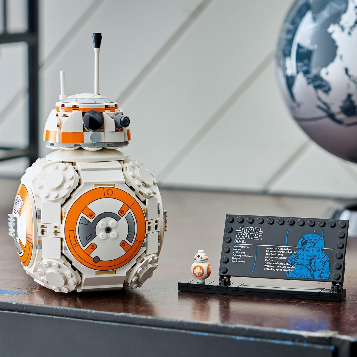 Droid LEGO BB-8 i mniejsza figurka BB-8 stoją na stole z tablicą informacyjną Star Wars i globusem w tle.