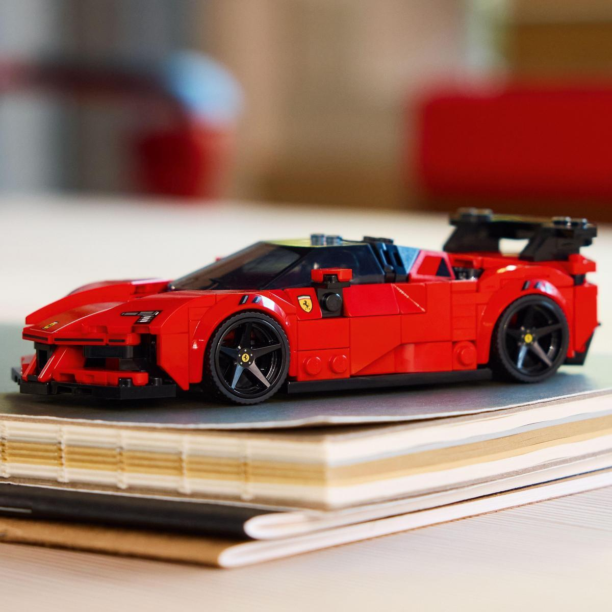 Czerwony samochód Ferrari Lego na książkach. Samochód ma czarne koła i żółty pasek. Tło jest rozmyte z czerwonym i białym.