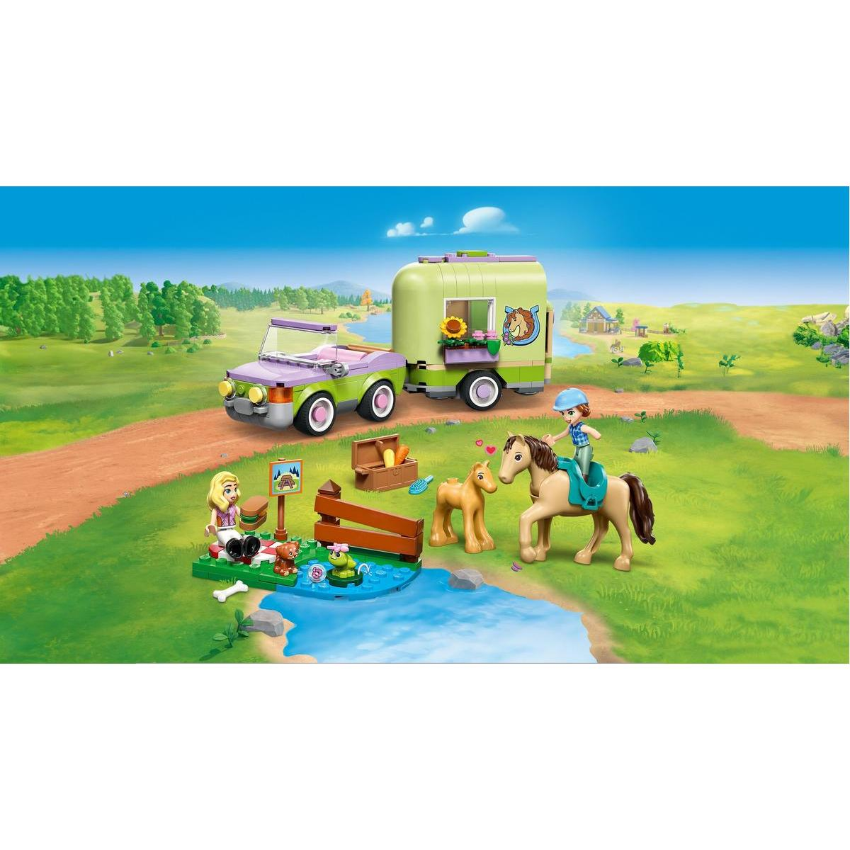 Scena z zabawkami przedstawia przyczepę dla koni, samochód, konie i figurki. Jedna figurka jedzie konno. Inne figurki są w pobliżu stawu z jedzeniem.