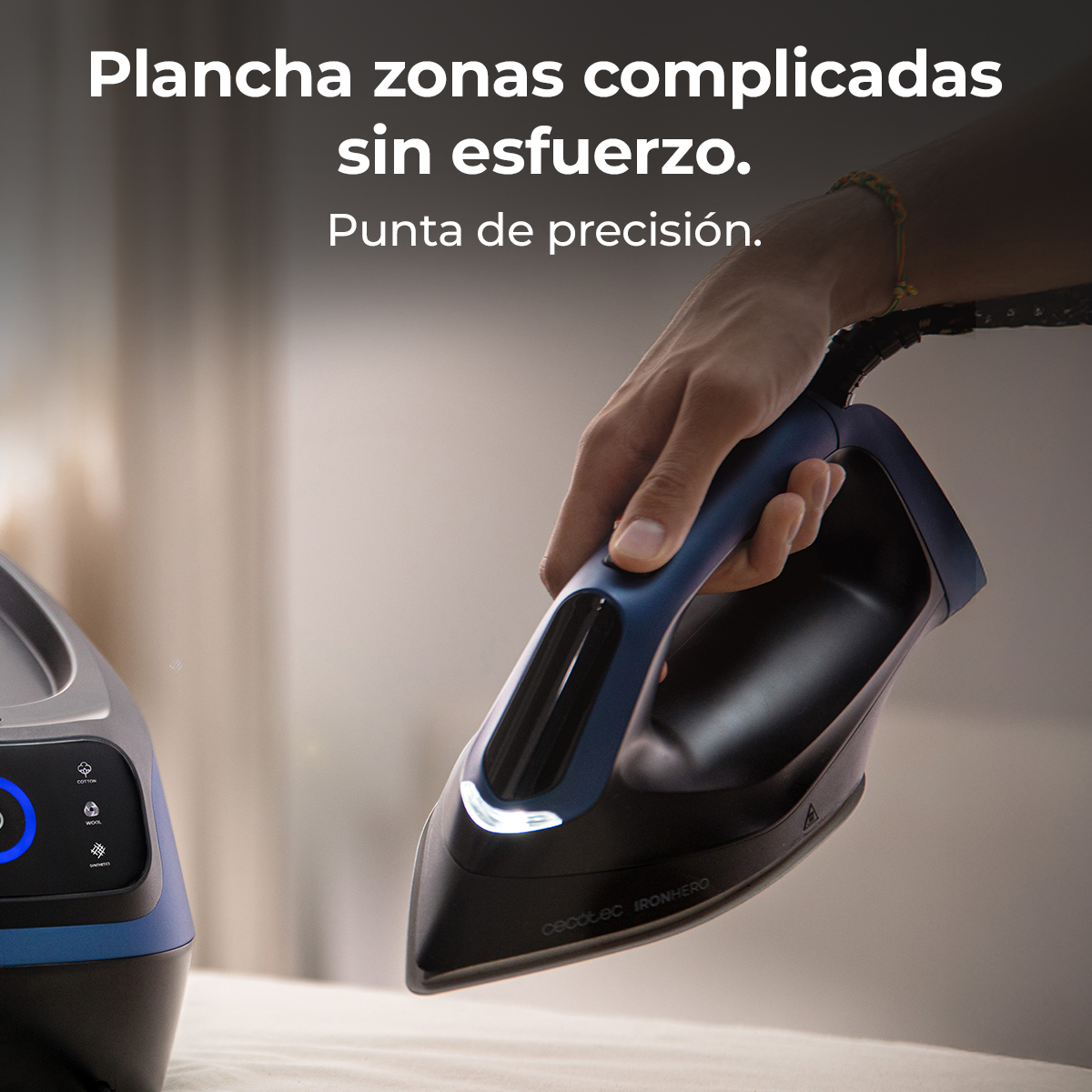 Una mano tiene un ferro da stiro blu e nero su tessuto bianco. Il ferro ha una punta e il marchio è visibile: Cecotec IRONHERO.