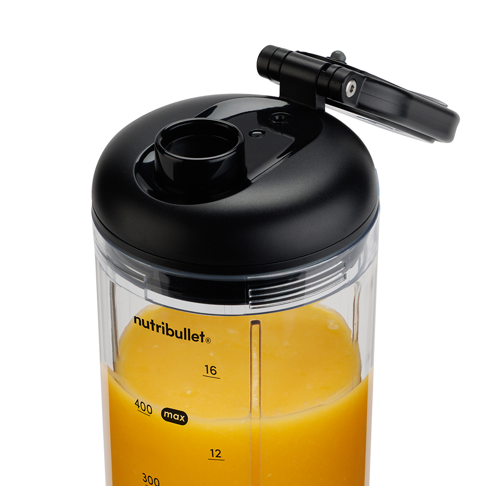 Een close-up van een zwarte Nutribullet blender met oranje vloeistof erin. Het deksel is open. De container heeft metingen.